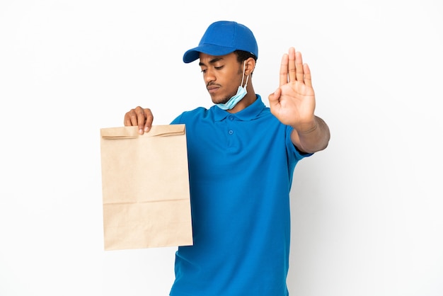 Hombre afroamericano tomando una bolsa de comida para llevar aislado sobre fondo blanco haciendo gesto de parada y decepcionado