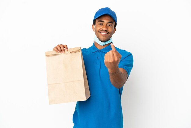 Hombre afroamericano tomando una bolsa de comida para llevar aislado sobre fondo blanco haciendo gesto que viene