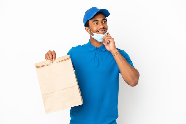 Hombre afroamericano tomando una bolsa de comida para llevar aislado sobre fondo blanco pensando en una idea mientras mira hacia arriba