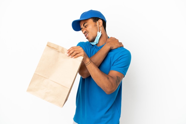 Hombre afroamericano tomando una bolsa de comida para llevar aislado sobre fondo blanco que sufre de dolor en el hombro por haber hecho un esfuerzo