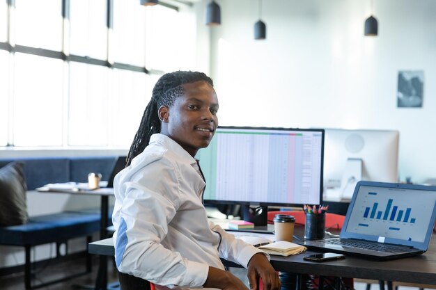 Hombre afroamericano trabajando en un escritorio en una oficina moderna de plano abierto con una taza de café de monitor de portátil