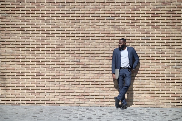 Un hombre afroamericano en un traje de pie cerca de la pared de ladrillos