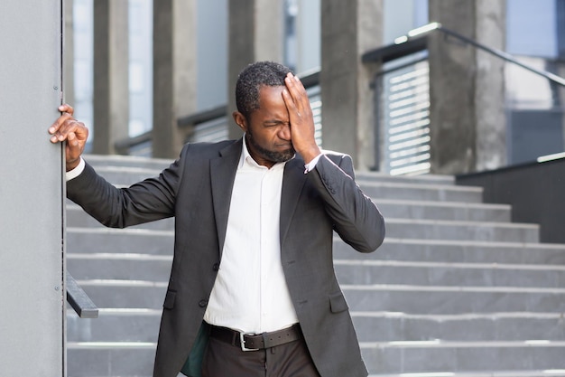 Un hombre afroamericano con traje se siente mal mareado y tiene dolor de cabeza pierde el conocimiento cierra su