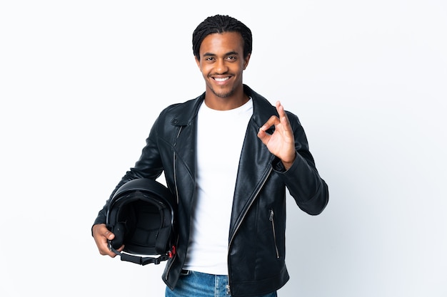 Hombre afroamericano con trenzas sosteniendo un casco de motocicleta en blanco mostrando signo ok con los dedos