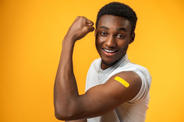 Hombre afroamericano vacunado que muestra su brazo contra el fondo amarillo
