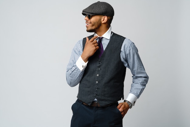 Hombre afroamericano vistiendo gorra, camisa y corbata sobre pared gris