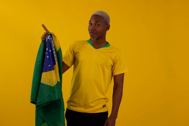 Hombre afrobrasileño partidario de la selección brasileña de fútbol en la copa 2022 con la bandera de Brasil y con expresiones faciales