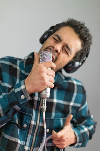 Hombre afrobrasileño vestido con camisa a cuadros cantando en un micrófono de condensador