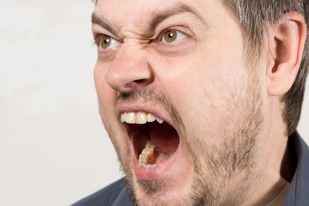 Un hombre agresivo enojado grita con la boca abierta.