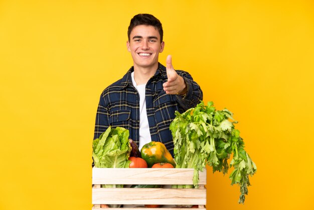 Hombre agricultor adolescente con verduras recién cortadas en una caja de apretón de manos después de un buen trato