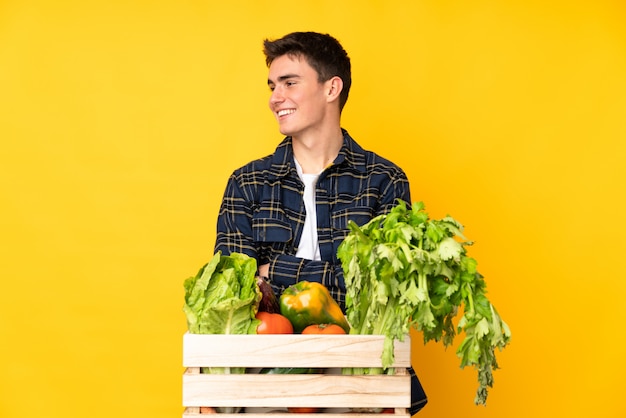 Hombre agricultor adolescente con verduras recién cortadas en una caja mirando hacia un lado