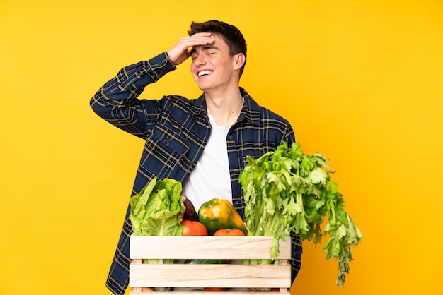 Hombre agricultor adolescente con verduras recién cortadas en una caja riendo