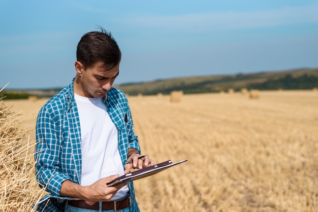 Hombre agricultor con tableta en mano, jeans y camisa en el campo, cosecha, henificación