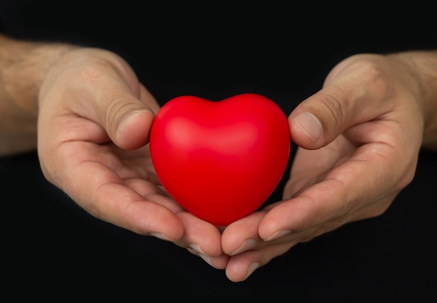 Hombre ahuecando el corazón rojo sobre fondo oscuro. Concepto de personas, relaciones, salud y amor.