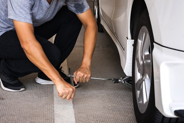 Foto hombre ajustando el tornillo de gato de un automóvil para subir de nivel para cambiar el neumático del automóvil o el mantenimiento