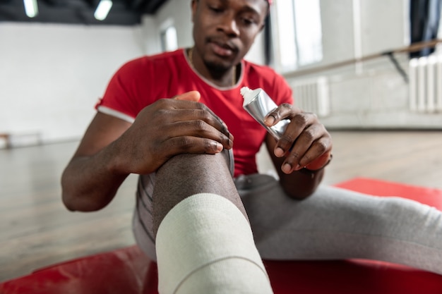 Hombre de ajuste enfocado adjuntando crema de calentamiento a las articulaciones lesionadas