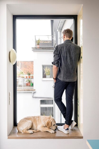 Hombre al teléfono parado en la ventana al lado del perro