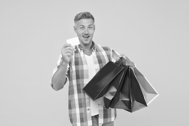 Foto hombre alegre adicto a las compras compra muchos paquetes de regalo en el centro comercial y muestra la tarjeta de visita el lunes cibernético