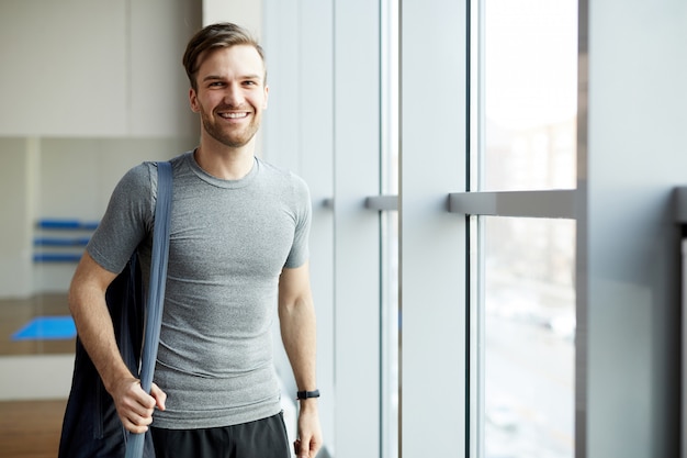 Hombre alegre con bolsa de colchoneta de yoga