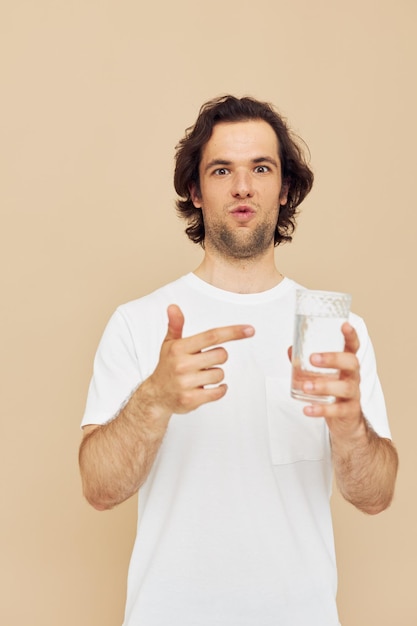 Hombre alegre con una camiseta blanca con una taza en la mano de fondo beige