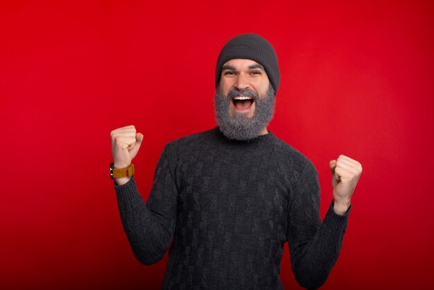 Hombre alegre celebrando el éxito sobre el espacio rojo, hombre con barba blanca