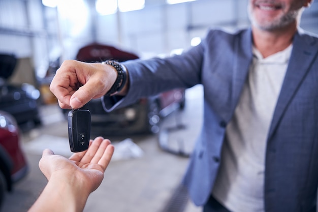 Hombre alegre dando la llave del coche inteligente al mecánico en la estación de servicio