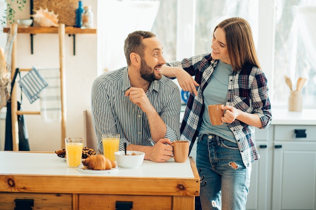 Hombre alegre disfrutando de té y una mujer sonriente poniendo un codo sobre su hombro