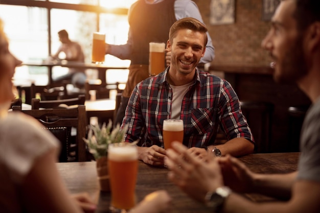 Hombre alegre divirtiéndose mientras pasa tiempo con amigos en un pub y bebiendo cerveza