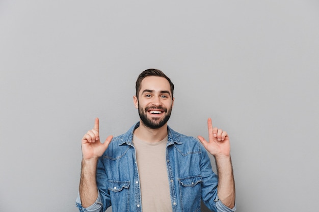 Hombre alegre emocionado vestido con camisa aislado sobre pared gris, apuntando al espacio de copia