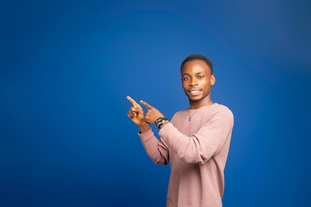 Un hombre alegre está de pie con el brazo levantado y una sonrisa dentada aislada contra un impresionante fondo azul mira a la cámara apuntando en dirección al éxito y la felicidad