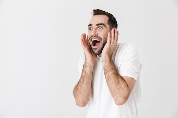 Hombre alegre guapo con camiseta en blanco que se encuentran aisladas sobre la pared blanca, gritando