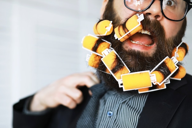 Hombre alegre hipster con rulos en la barba. Hombre sorprendido con gafas mira al frente.