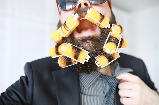 Hombre alegre hipster con rulos en la barba. Hombre sorprendido con gafas mira al frente.