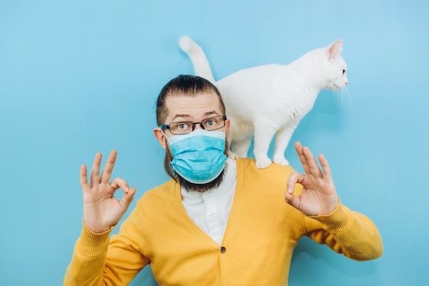 Un hombre alegre con una máscara médica con un gato blanco en el hombro. Pandemia COVID 2019. Pet.