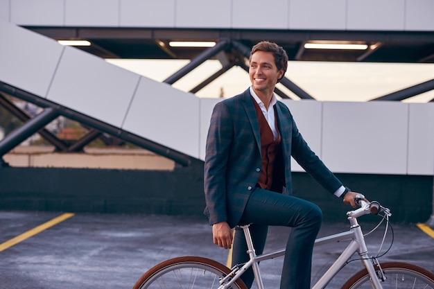 Hombre alegre moderno con bicicleta en el centro de negocios