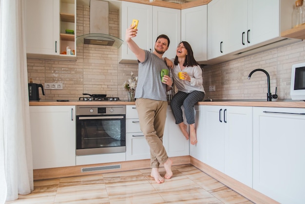 Hombre alegre con mujer tomando selfie en la cocina mientras bebe té concepto de hogar