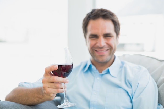 Hombre alegre que se relaja en el sofá con un vaso de vino tinto