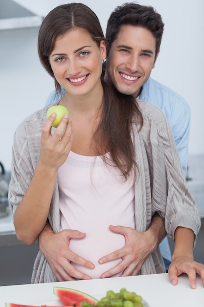 Hombre alegre que sostiene el vientre de su esposa embarazada