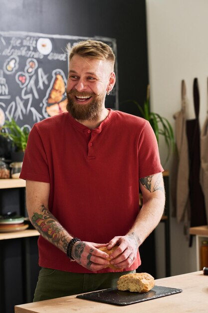 Hombre alegre rompiendo pan en la cocina