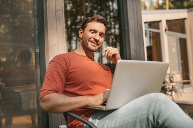 Hombre alegre sentado con portátil al aire libre