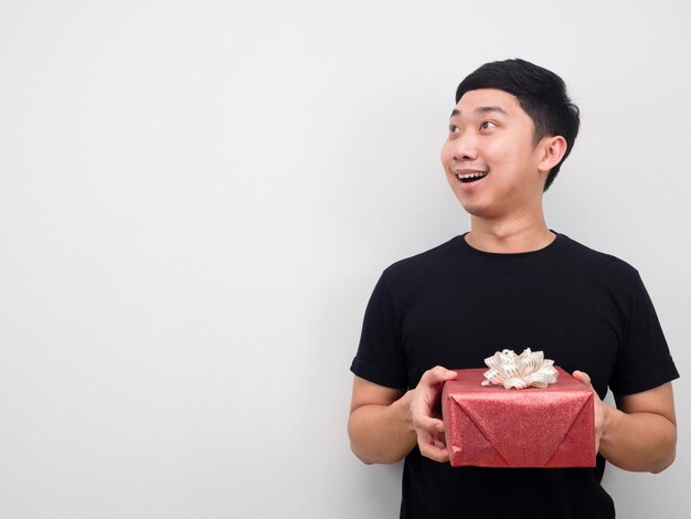 Hombre alegre sosteniendo caja de regalo y mirando el fondo blanco del espacio de copia