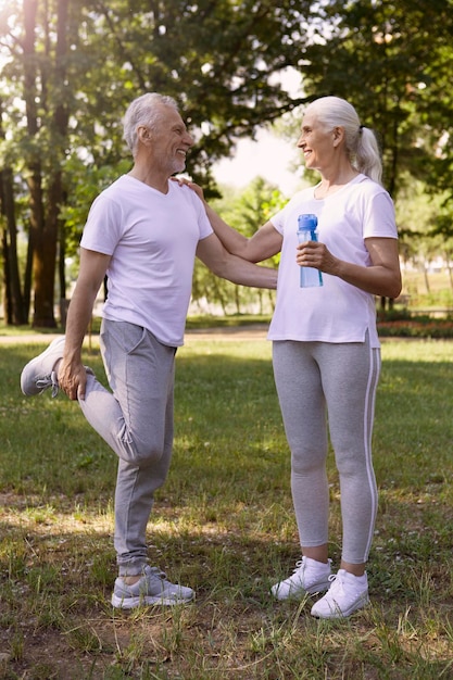 Foto hombre alegre sosteniendo su tobillo y estirando las piernas mientras su esposa toca tiernamente su hombro y sonríe