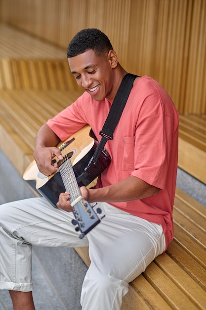 Hombre alegre tocando la guitarra sentado al aire libre