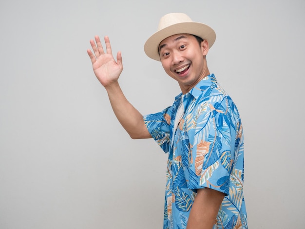 El hombre alegre usa sombrero, camisa de playa, da la vuelta y saluda.