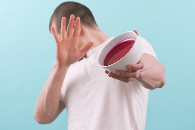 Un hombre se aleja de un plato con una gelatina roja dulce sobre un fondo azul Sabor Frescura Refresco afrutado Color Confección Fresco Aislado Comer Color Plato