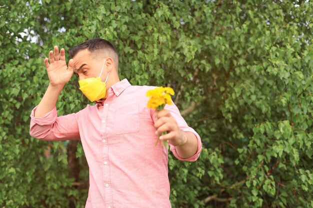 Hombre alérgico con mascarilla médica en la cara sosteniendo un ramo de flores