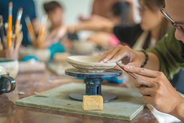 Hombre alfarero trabajando en la rueda de alfarero haciendo vasija de cerámica de arcilla en el concepto de arte del taller de cerámica Enfoque mano joven adjuntando parte del producto de arcilla al futuro producto de cerámica Taller de cerámica