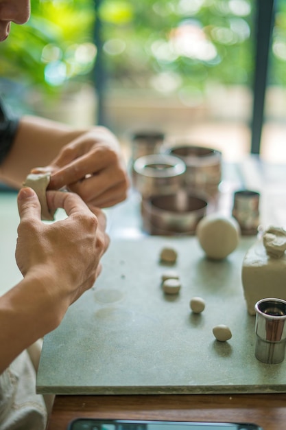 Hombre alfarero trabajando en la rueda de alfarero haciendo vasija de cerámica de arcilla en el concepto de arte del taller de cerámica Enfoque mano joven adjuntando parte del producto de arcilla al futuro producto de cerámica Taller de cerámica