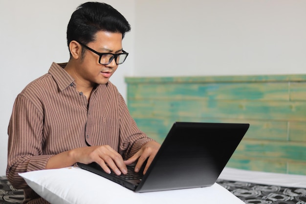 Hombre con almohada usando computadora portátil en el dormitorio