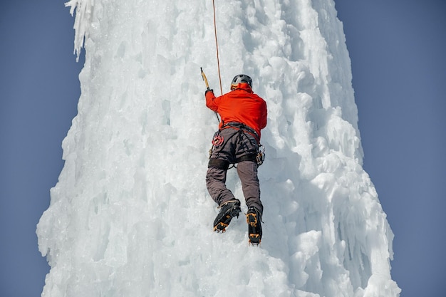 Hombre alpinista con hacha de herramientas de hielo trepando una gran pared de hielo. Retrato de deportes al aire libre.